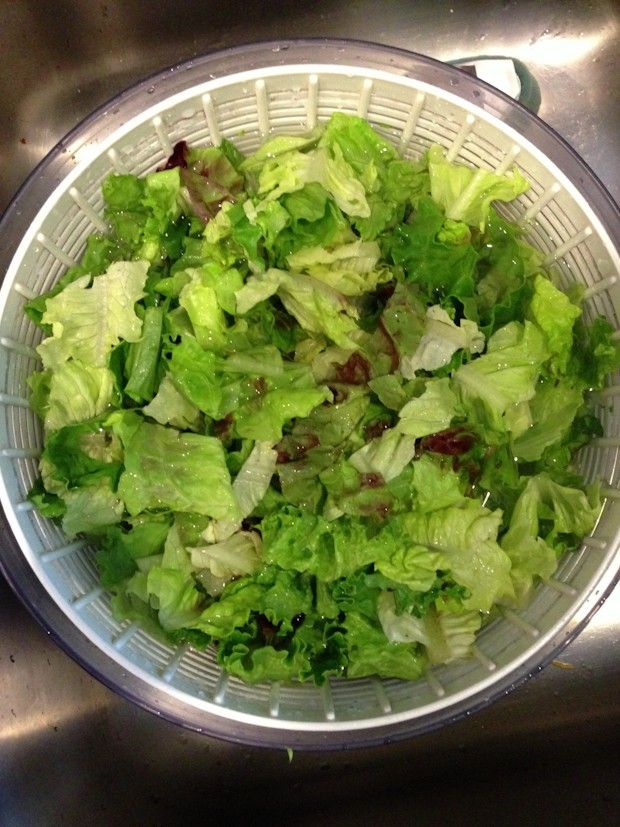 lettuce in a bowl sitting on top of a sink next to a faucet