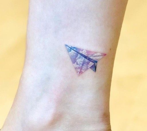 a small origami airplane tattoo on the ankle