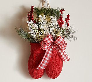 a christmas stocking hanging on the wall with flowers and greenery in red mittens