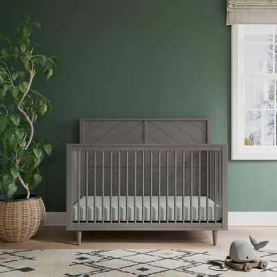 a baby crib in a green room with a potted plant on the floor