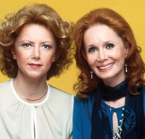 two women standing next to each other in front of a yellow background, one with red hair and the other with blue eyes