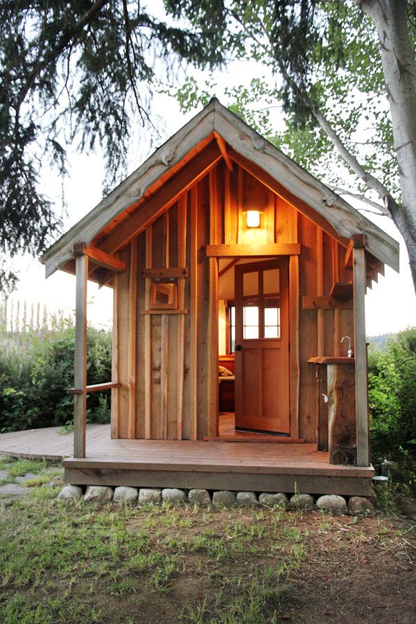 a small wooden cabin sitting on top of a lush green field next to a tree