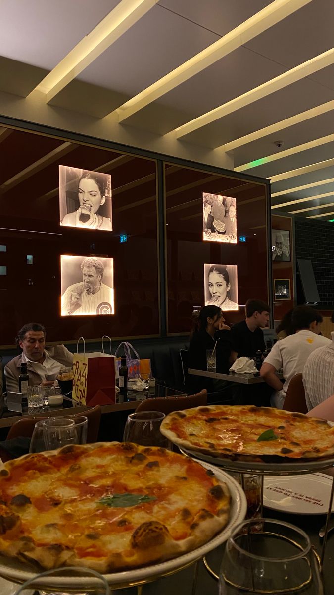 two large pizzas sitting on top of pans in front of people at tables