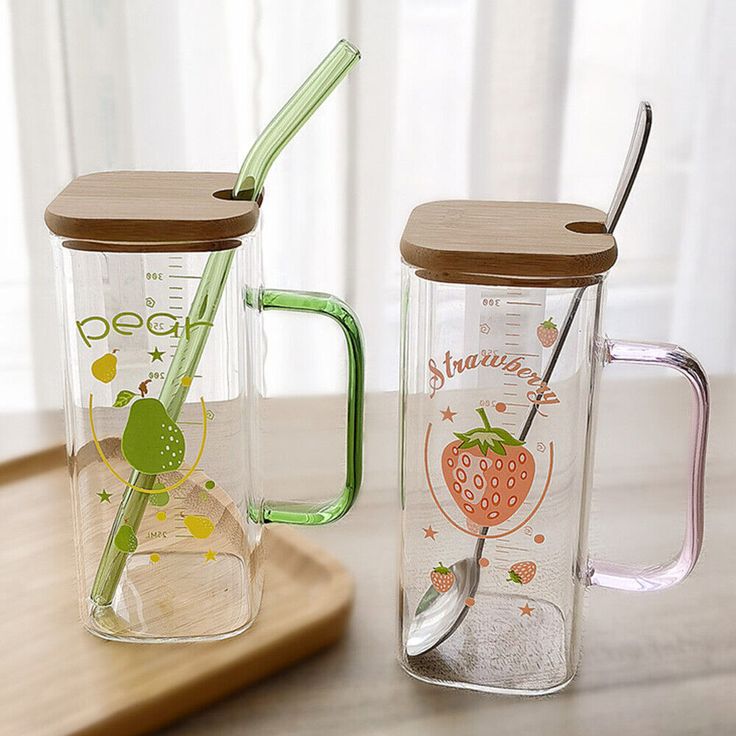 two glass mugs with strawberries on them are sitting on a wooden tray next to each other