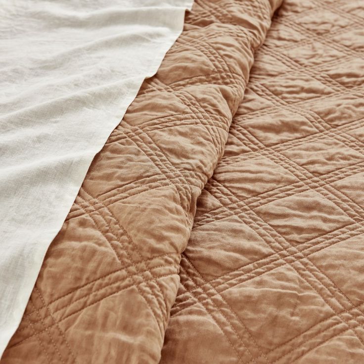 an unmade bed with brown and white quilting on it's side, next to a pillow