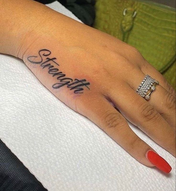 a woman's hand with the word strength tattooed on her left thumb and red nail polish