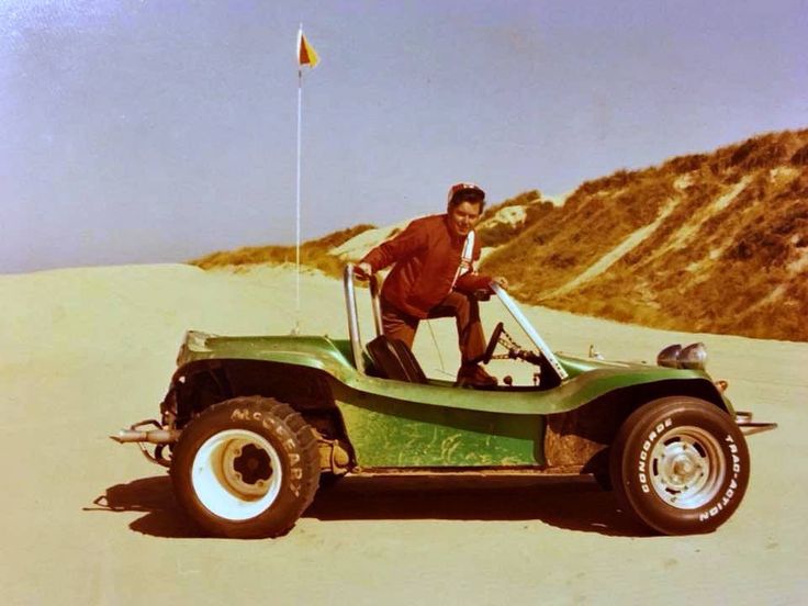 a man standing on top of a green car in the sand