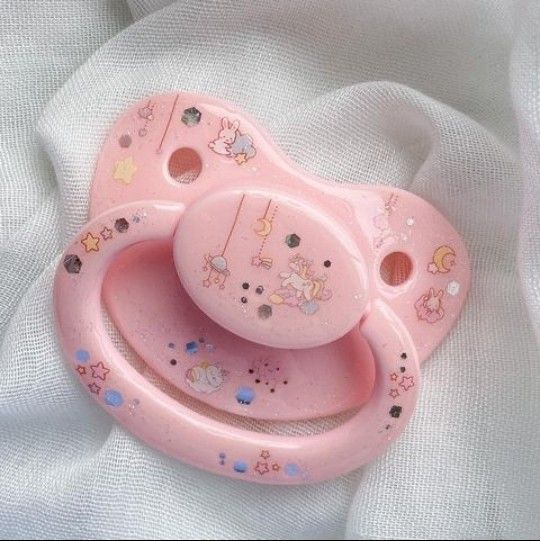 a pink baby pacifier sitting on top of a white sheet with stars and unicorns