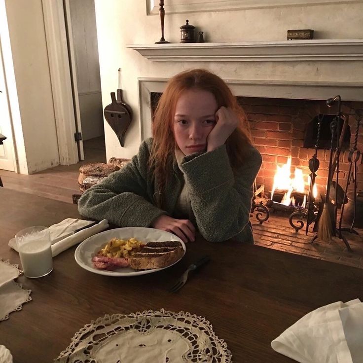 a woman sitting at a table with food in front of a fire place and fireplace