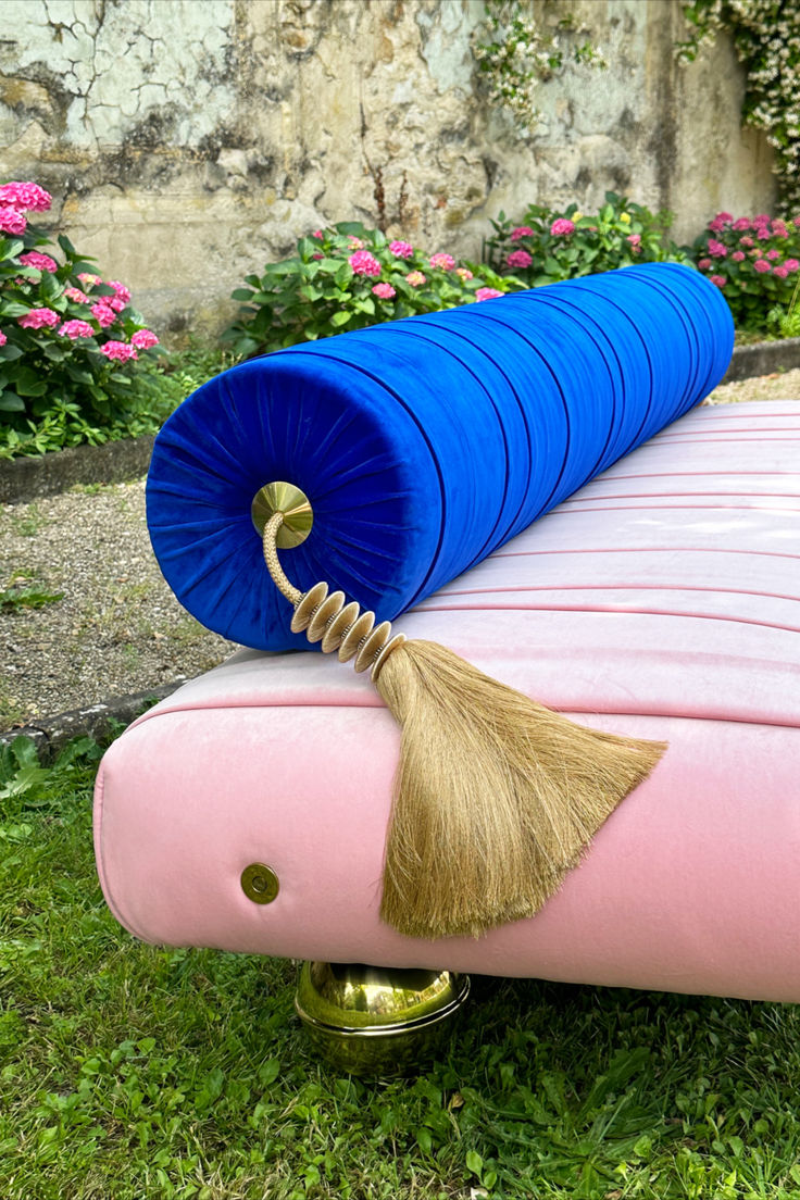 a pink and blue couch with a tassel on it's end sitting in the grass