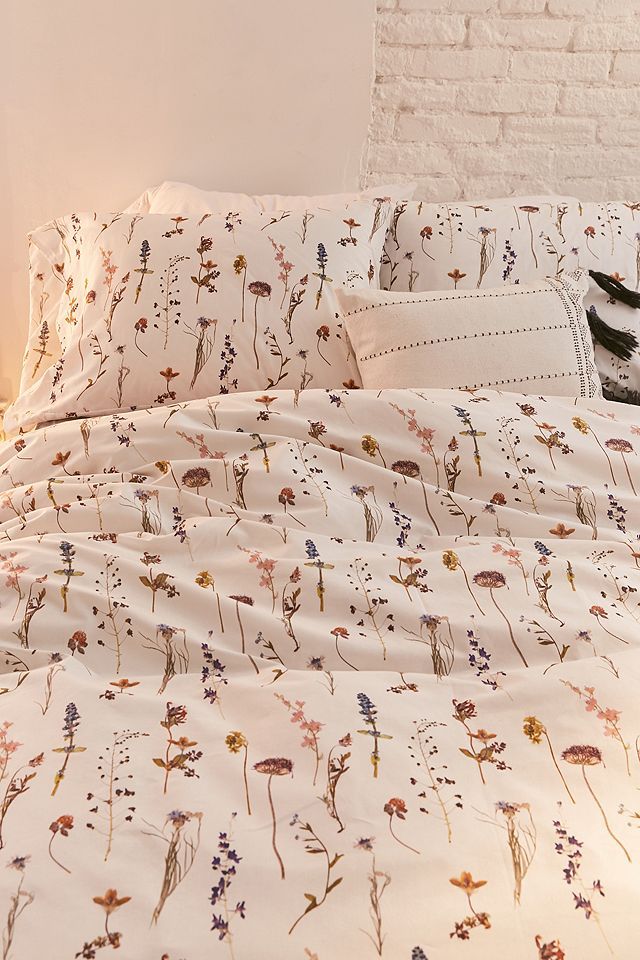 a cat is sitting on the edge of a bed with white sheets and floral print