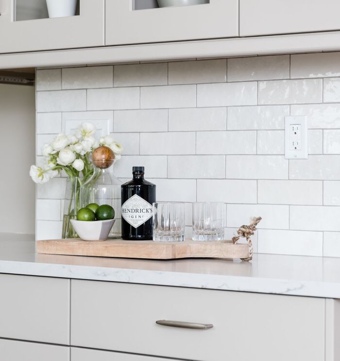 a kitchen counter with flowers and glasses on it, next to a bottle of gin