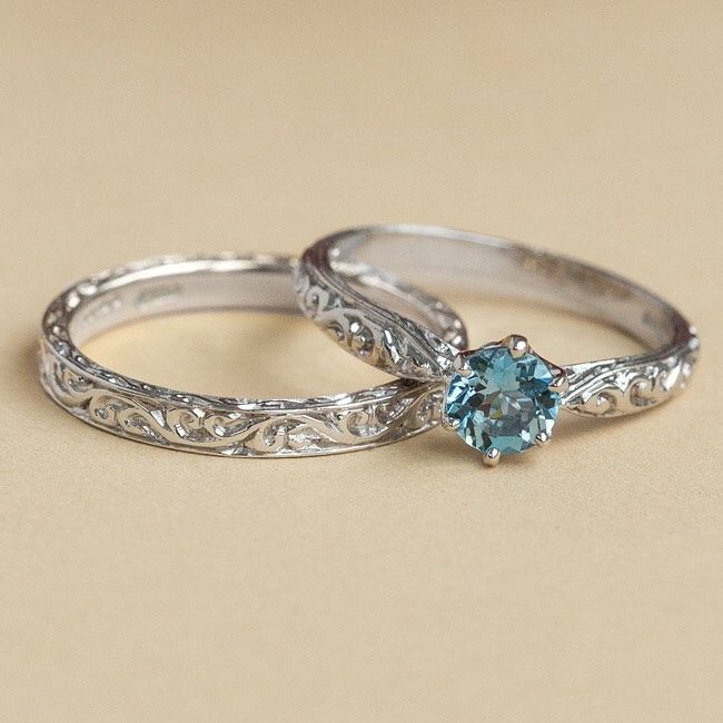 two wedding rings with blue topaz and filigrees on the sides, sitting next to each other