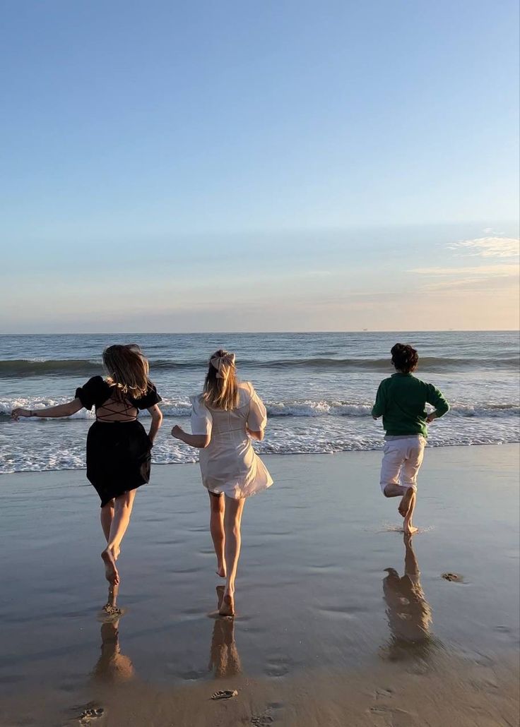 three people are running on the beach together