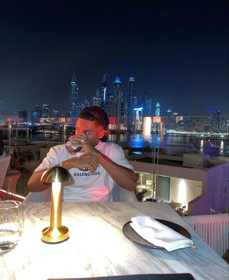 a man sitting at a table drinking from a wine glass in front of a city skyline