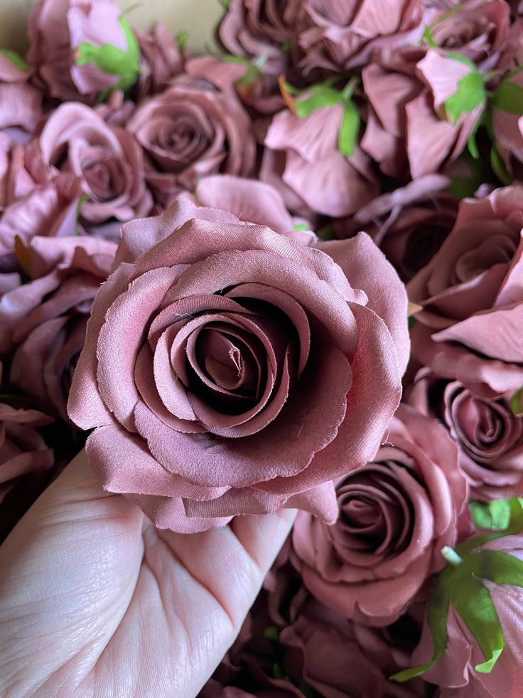 a person's hand holding a pink rose in the middle of a bouquet of purple flowers