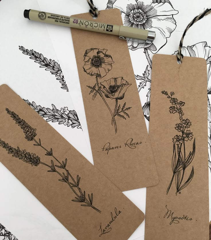 three tags with flowers drawn on them next to a marker and some markers in the background