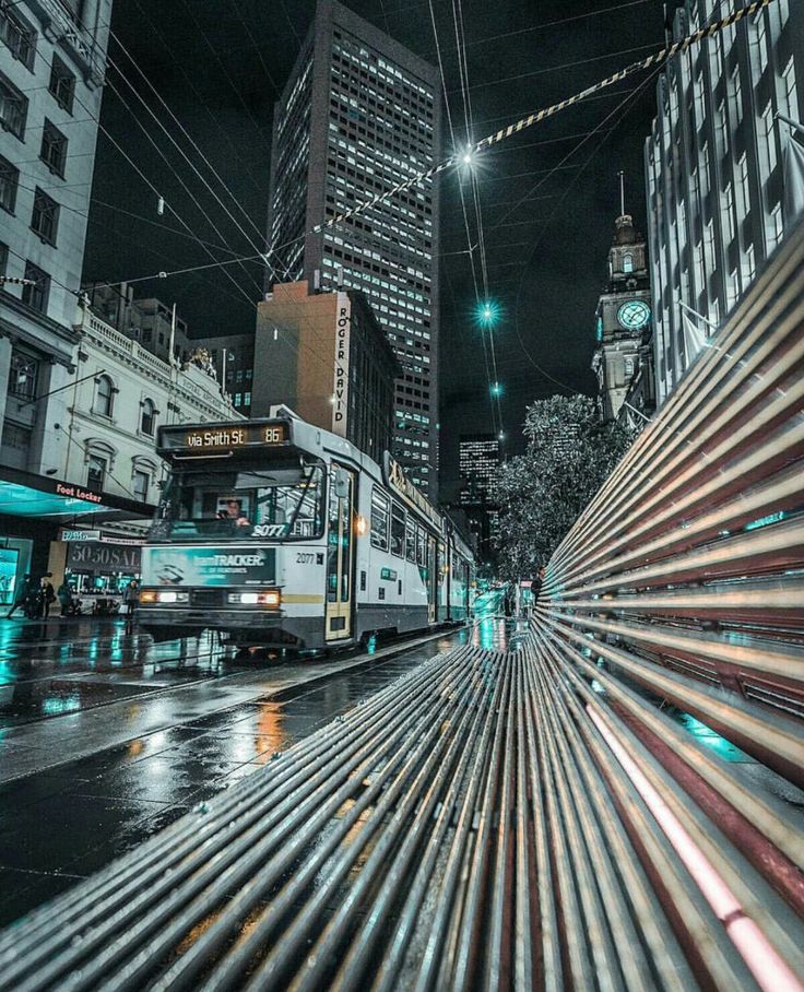 a city bus driving down a street next to tall buildings at night with ...