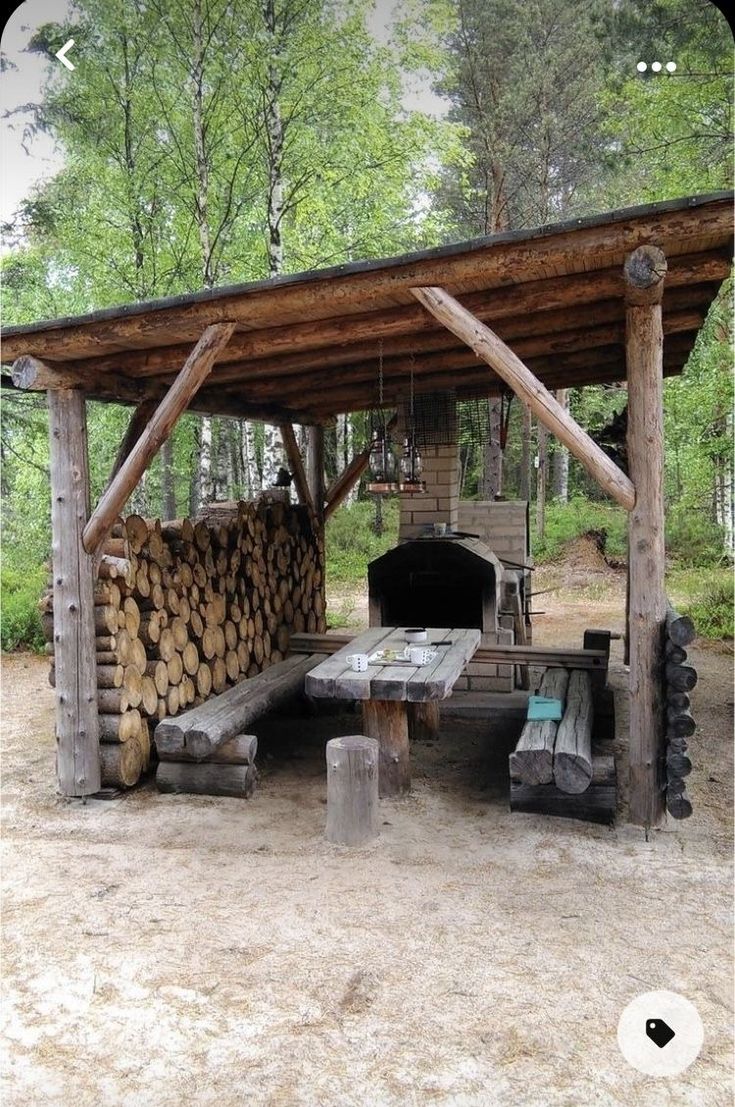 an outdoor grill made out of logs in the middle of a forest with picnic tables and benches