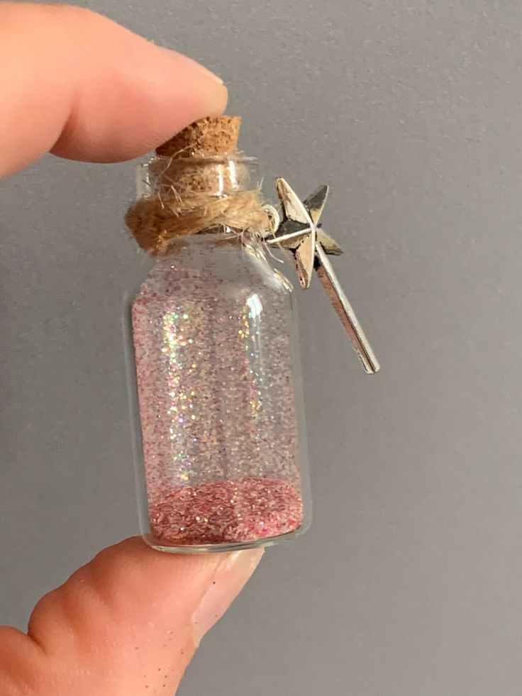 a hand holding a tiny glass bottle filled with glitter and a cross on the top