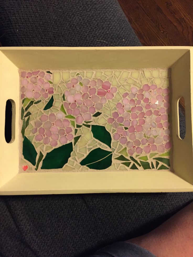 a white tray with pink flowers and green leaves on the bottom is sitting on a person's lap