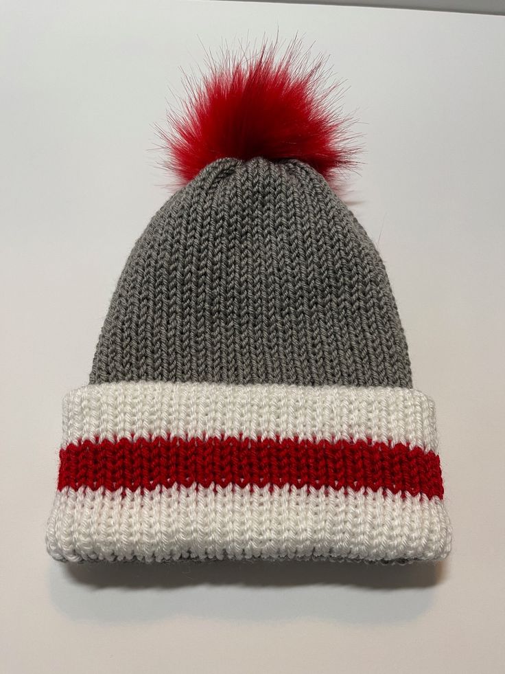 a knitted hat with a red and white stripe on the front, and a pom - pom at the top