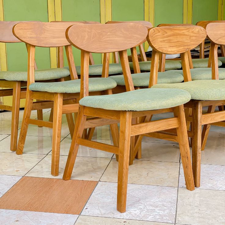 six wooden chairs with green upholstered seats in front of a yellow and green wall