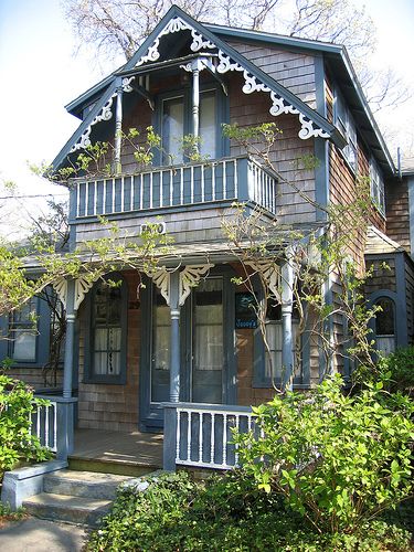 an old house is painted blue and has white trim on the front porch, along with several bushes