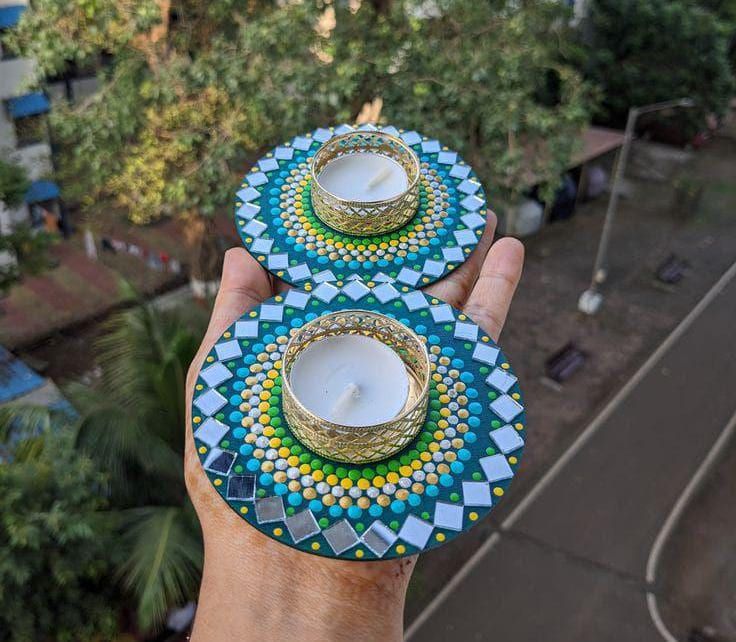 two hand holding plates with candles on them in the middle of a street and trees