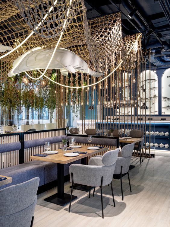 the interior of a restaurant with blue and white chairs, wooden tables and plants hanging from the ceiling