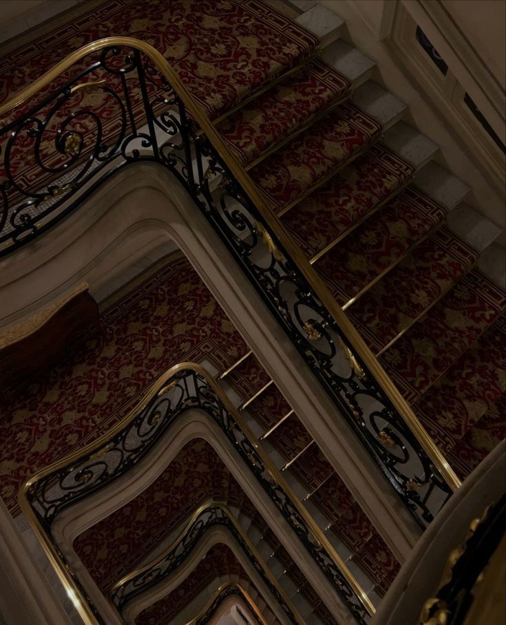 an ornate stair case in a building with red and gold wallpaper