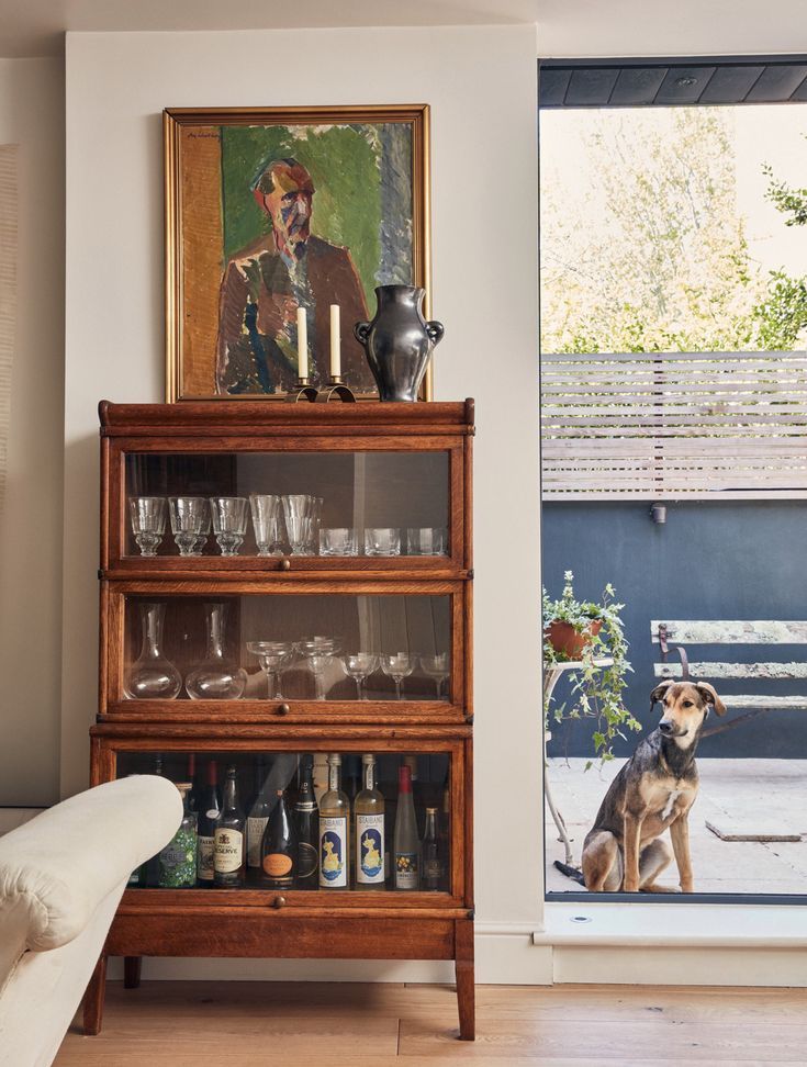 a dog sitting on the floor in front of a shelf with wine glasses and liquor bottles