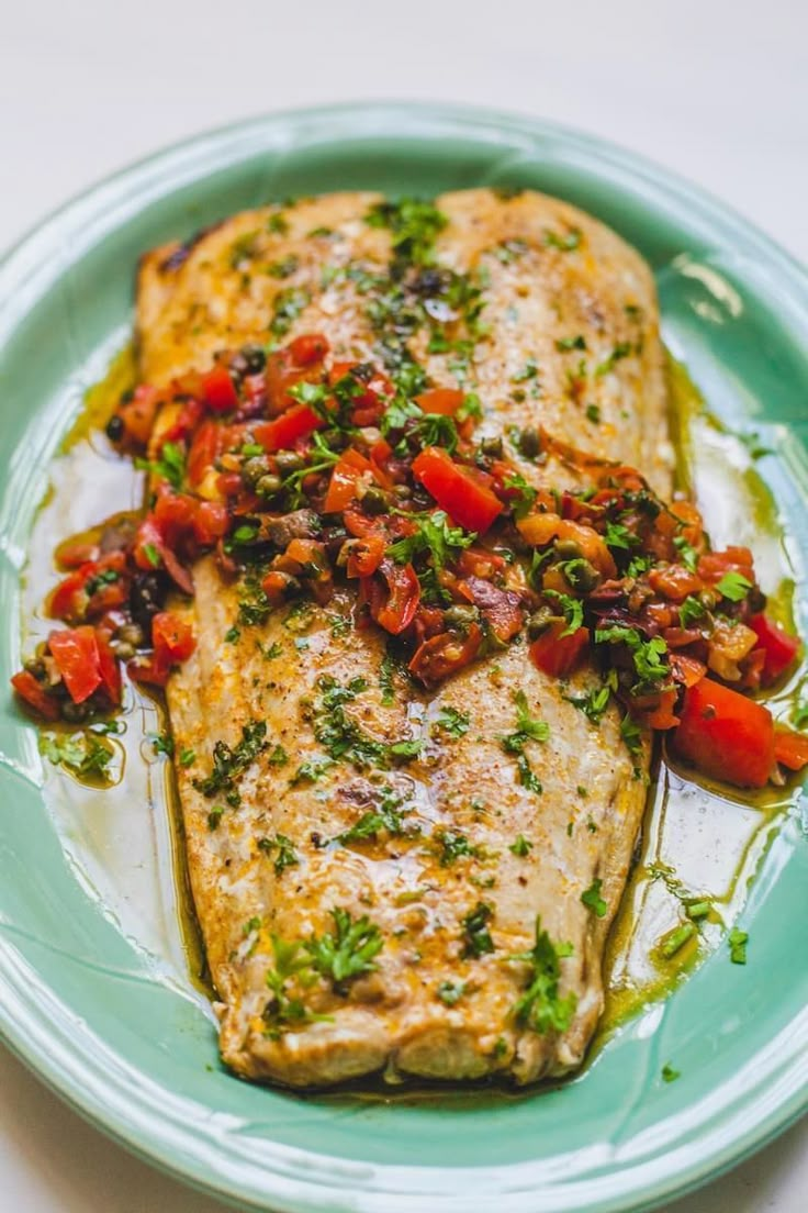 a piece of fish on a plate with tomatoes and herbs