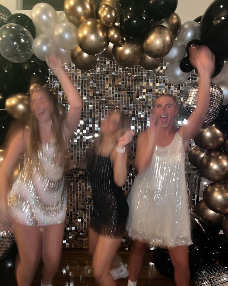 three women in sequin dresses are posing for the camera with balloons and streamers behind them