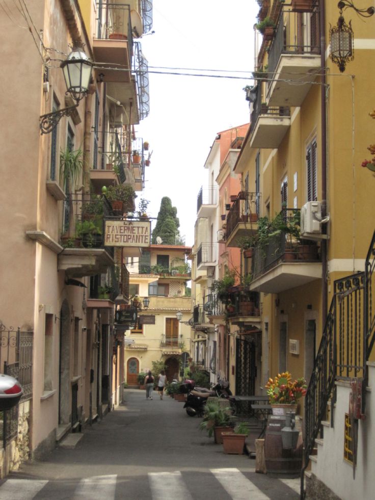 an alley way with several buildings and flowers on the balconies