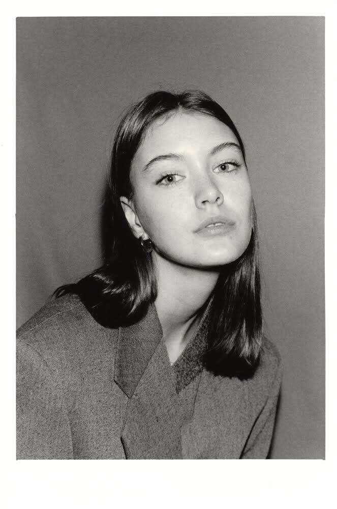 a black and white photo of a woman with long hair wearing a suit looking at the camera