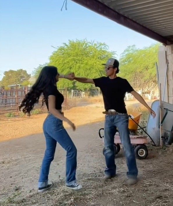 a man and woman dancing in front of a horse trailer with a wheelbarrow behind them