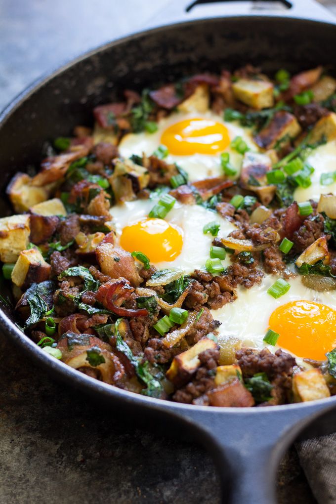 an iron skillet filled with eggs, sausage and other food on top of a table