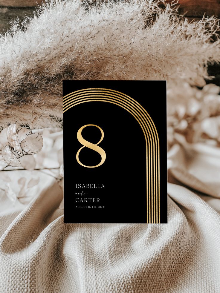 a black and gold wedding card with the letter s on it sitting on a bed