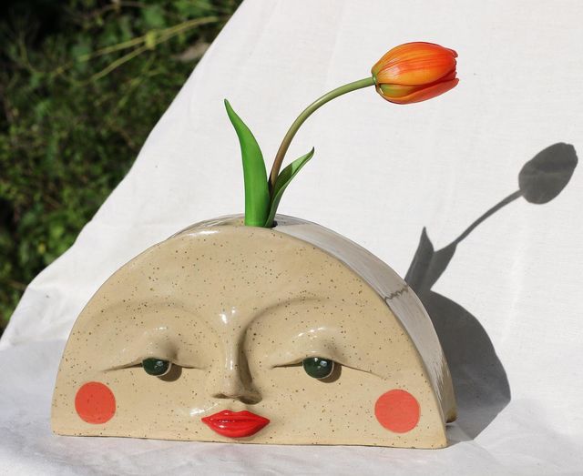 a ceramic vase with a flower in the shape of a woman's face on a white sheet