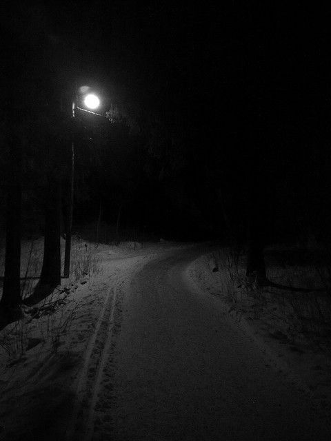 a dark road in the woods at night with a street light on it's side