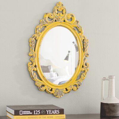 a yellow mirror sitting on top of a table next to a stack of books and a vase