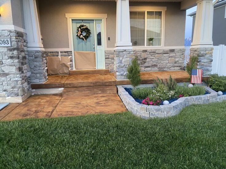 a front yard with grass and flowers in the foreground, an american flag wreath on the door