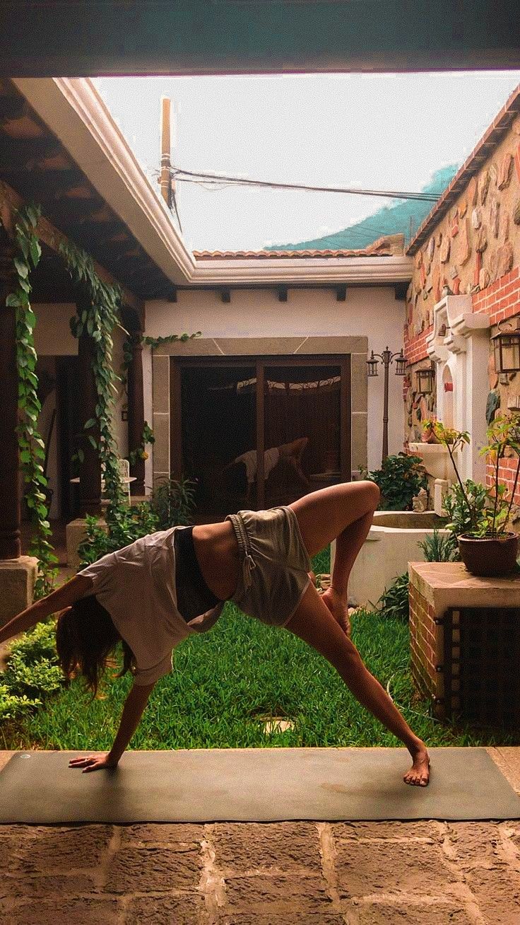 a woman is doing yoga outside in the yard with her hands on her hips and legs bent over her head