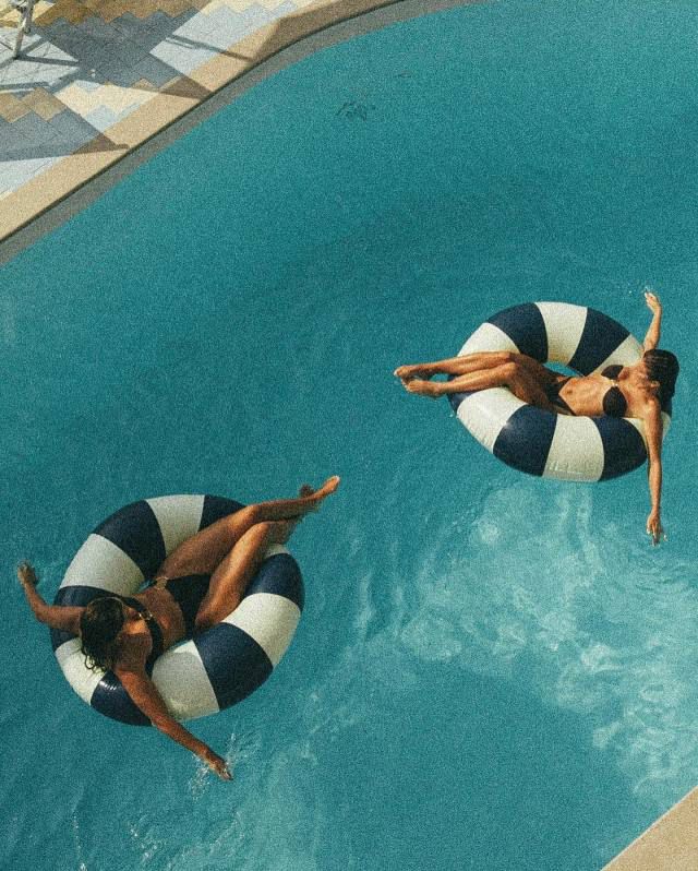 two people floating on inflatable rafts in a swimming pool with blue water