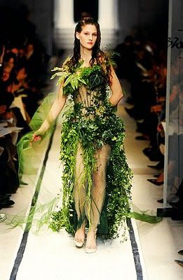 a woman is walking down the runway in a green dress with plants all over it