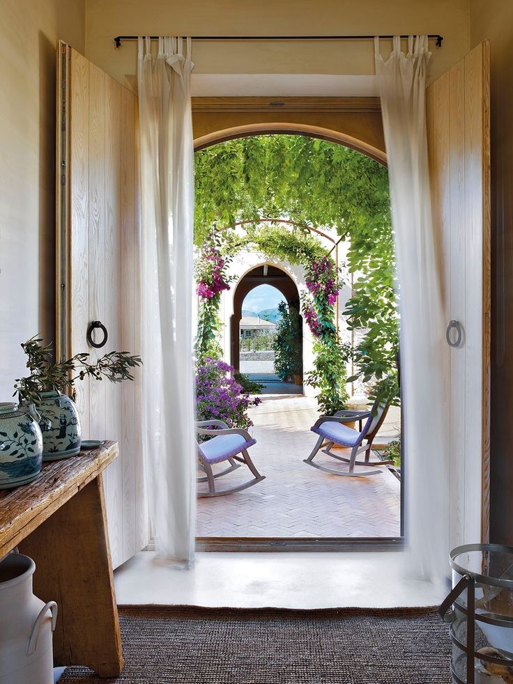 an open door leading to a patio with chairs and potted plants on either side