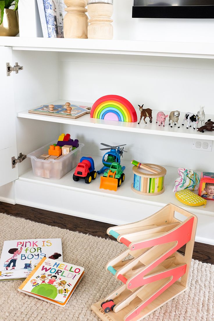 toys and books sit on the floor in front of a white bookcase with shelves