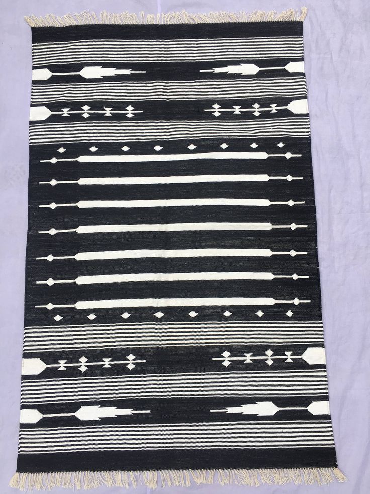 a black and white area rug with fringes on the bottom, in front of a light purple background