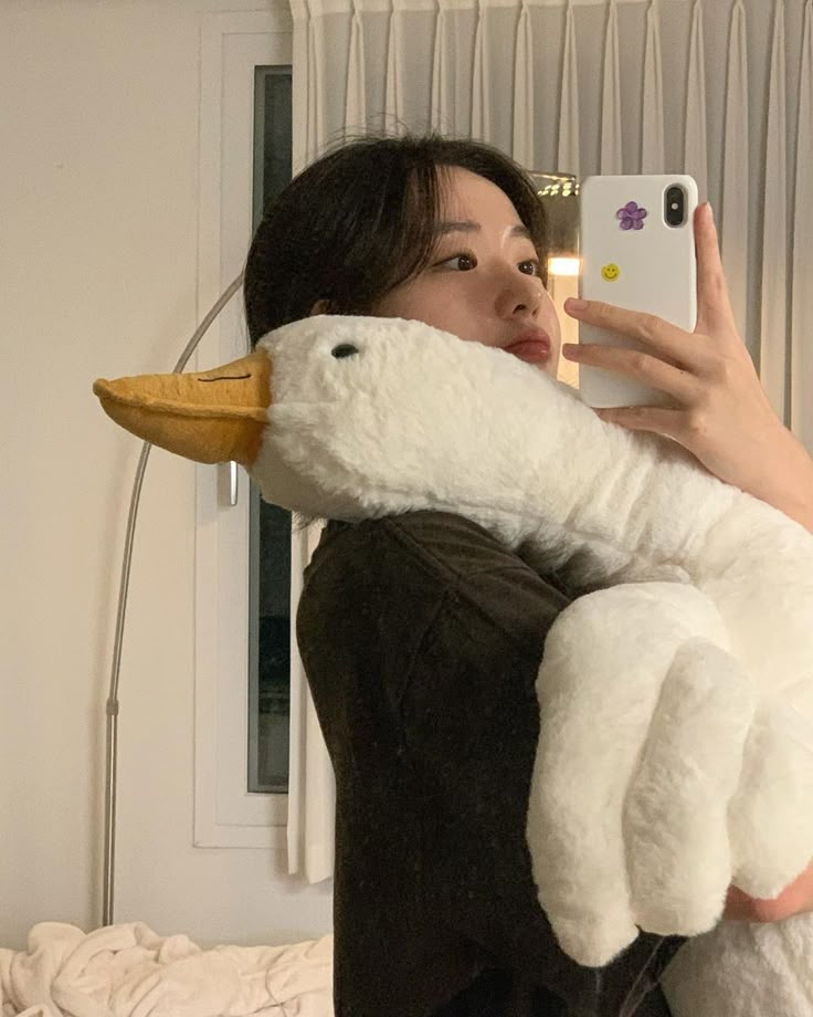 a woman is holding a stuffed animal and taking a selfie with her cell phone